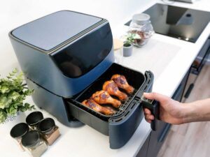 una friggitrice ad aria con il cestello pieno di cosce di pollo