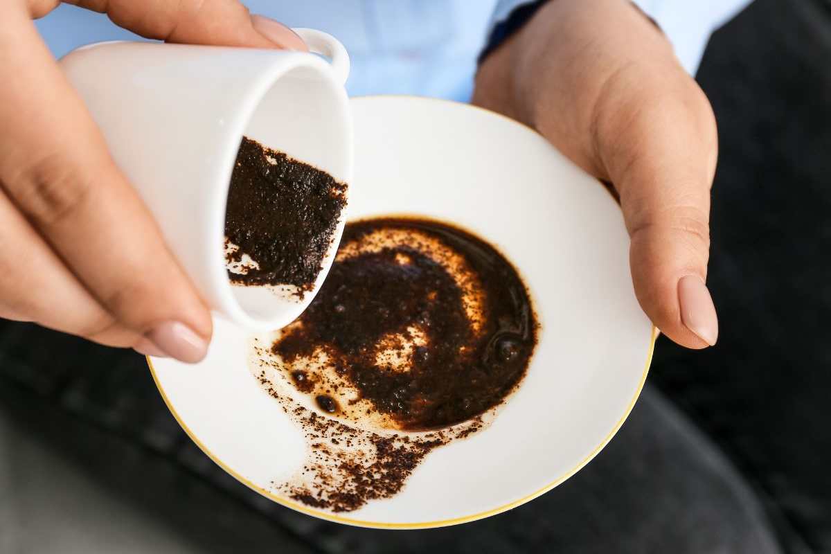 persona versa fondo di caffè su un piattino
