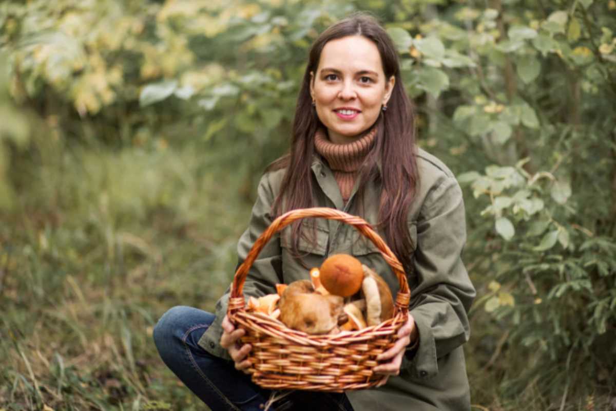 donna nel bosco che tiene un cestino pieno di funghi